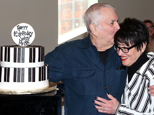 John Kander gives Chita Rivera a big kiss as they pose with his piano-themed birthday cake.