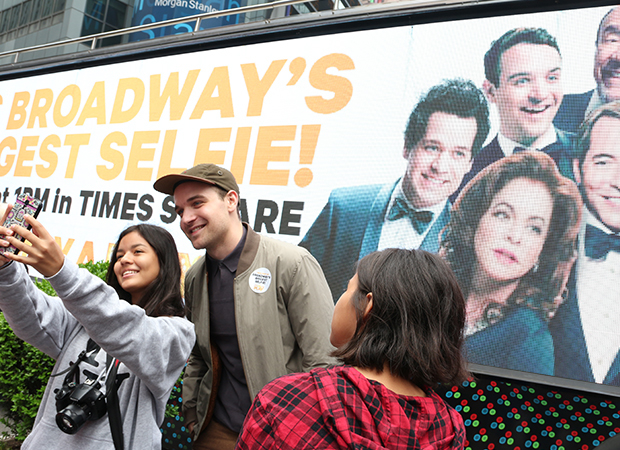 A passerby takes a selfie with Micah Stock in front of a bus bearing the It&#39;s Only a Play artwork.