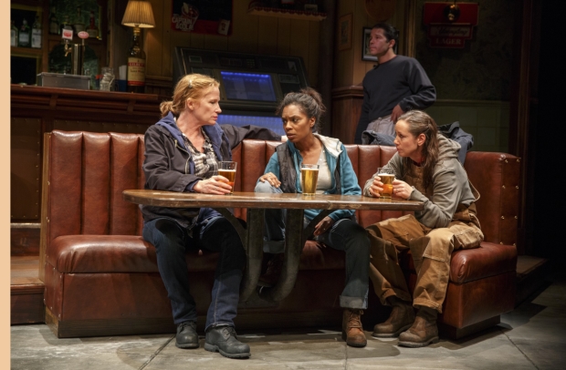 Tracey (Johanna Day), Cynthia (Michelle Wilson), and Jessie (Miriam Shor) enjoy a post-shift drink while Oscar (Carlo Albán, background) tidies the bar in Sweat.