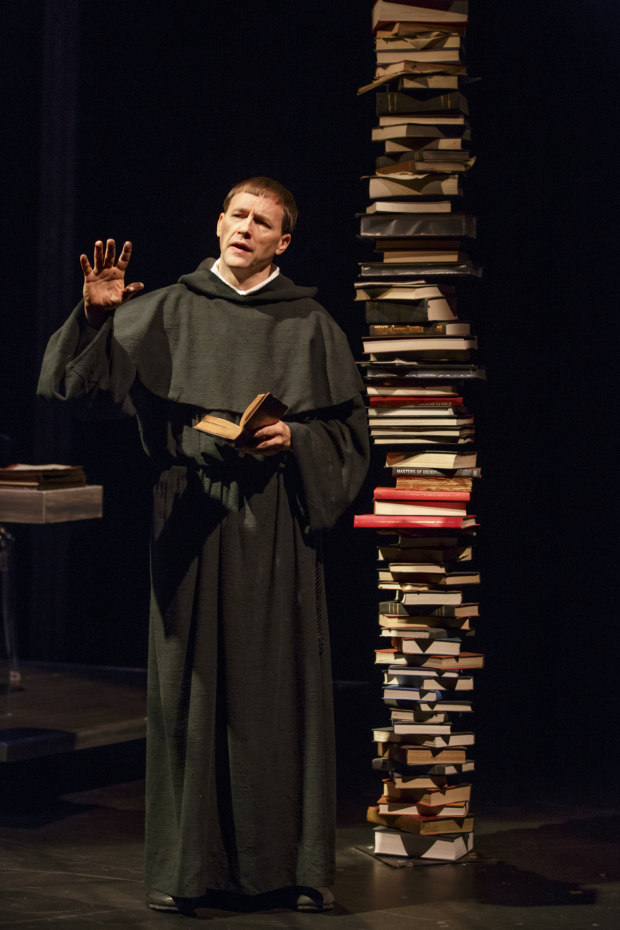 Martin Luther (Fletcher McTaggart) stands next to a giant stack of books about his life and legacy in Martin Luther on Trial.